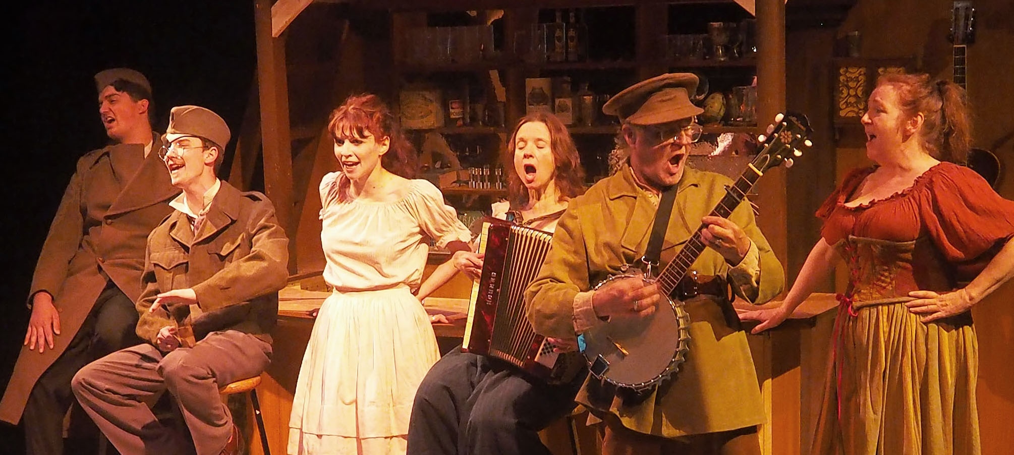 A group of performers sing and play instruments in a bar set. The atmosphere is of the early 1900s.