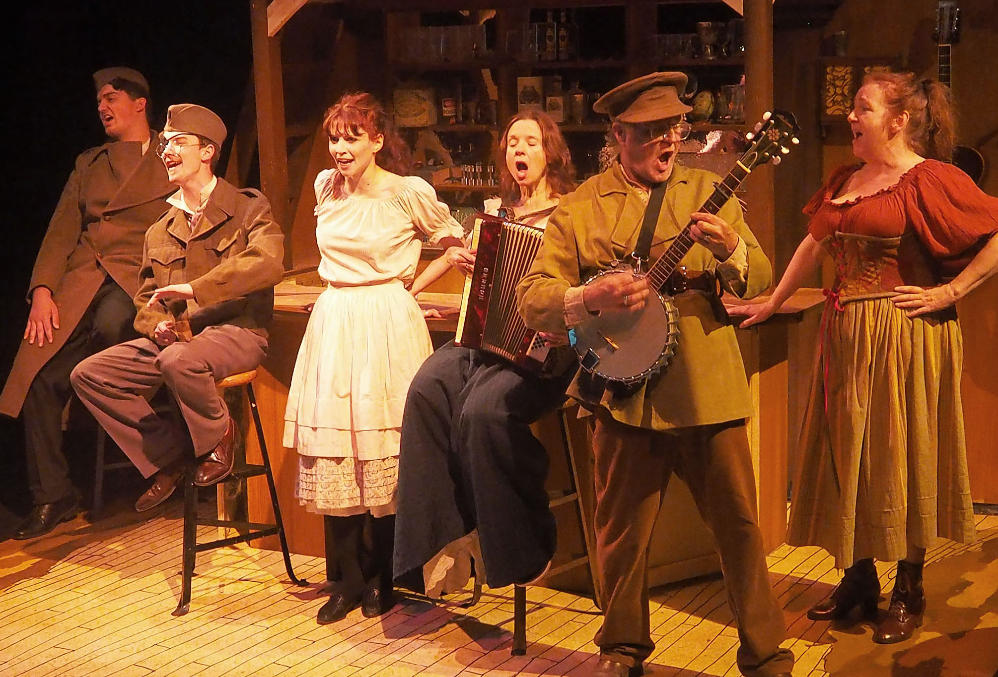 A group of performers sing and play instruments in a bar set. The atmosphere is of the early 1900s.
