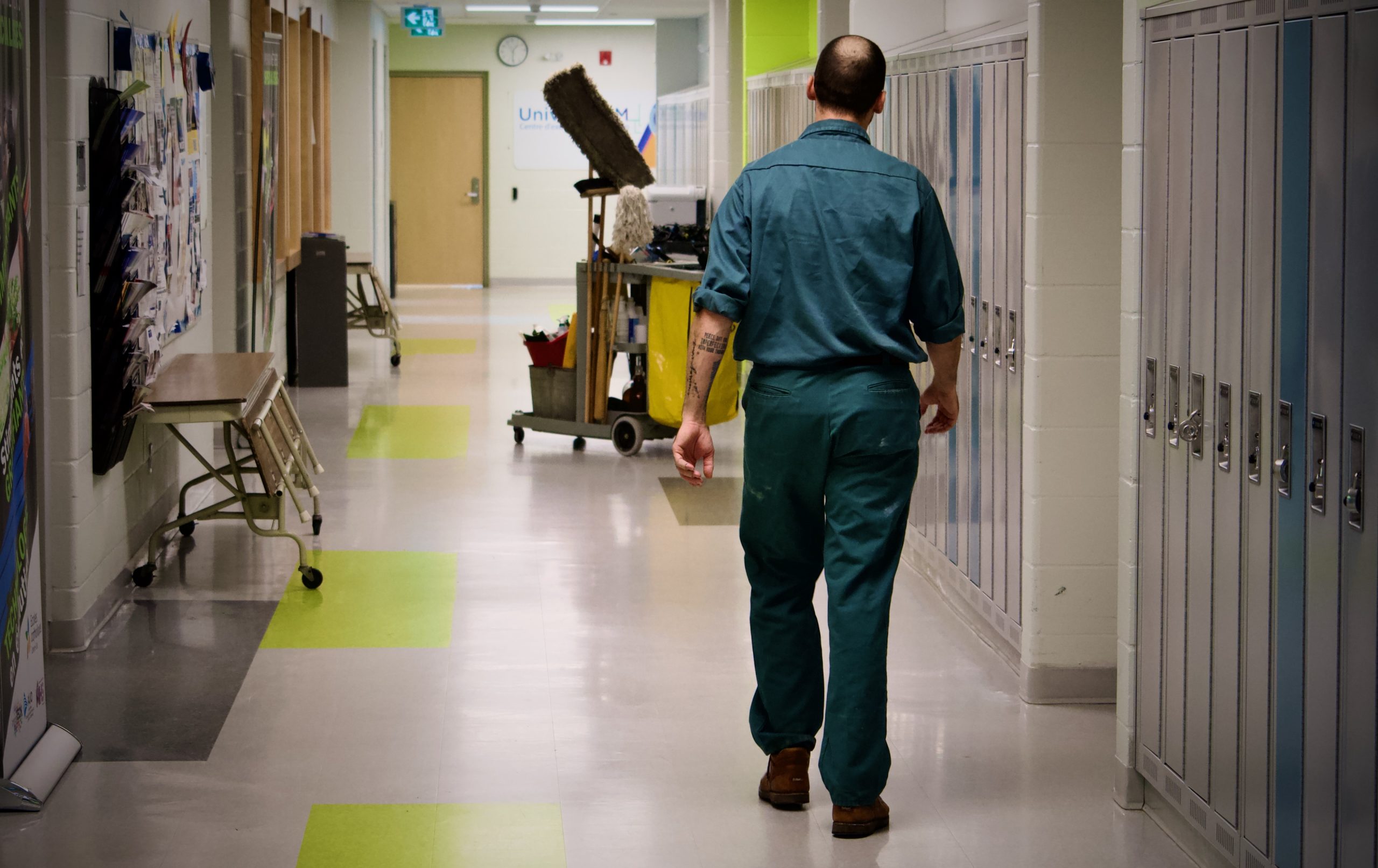 A school custodian walks down a hallway lined with lockers.