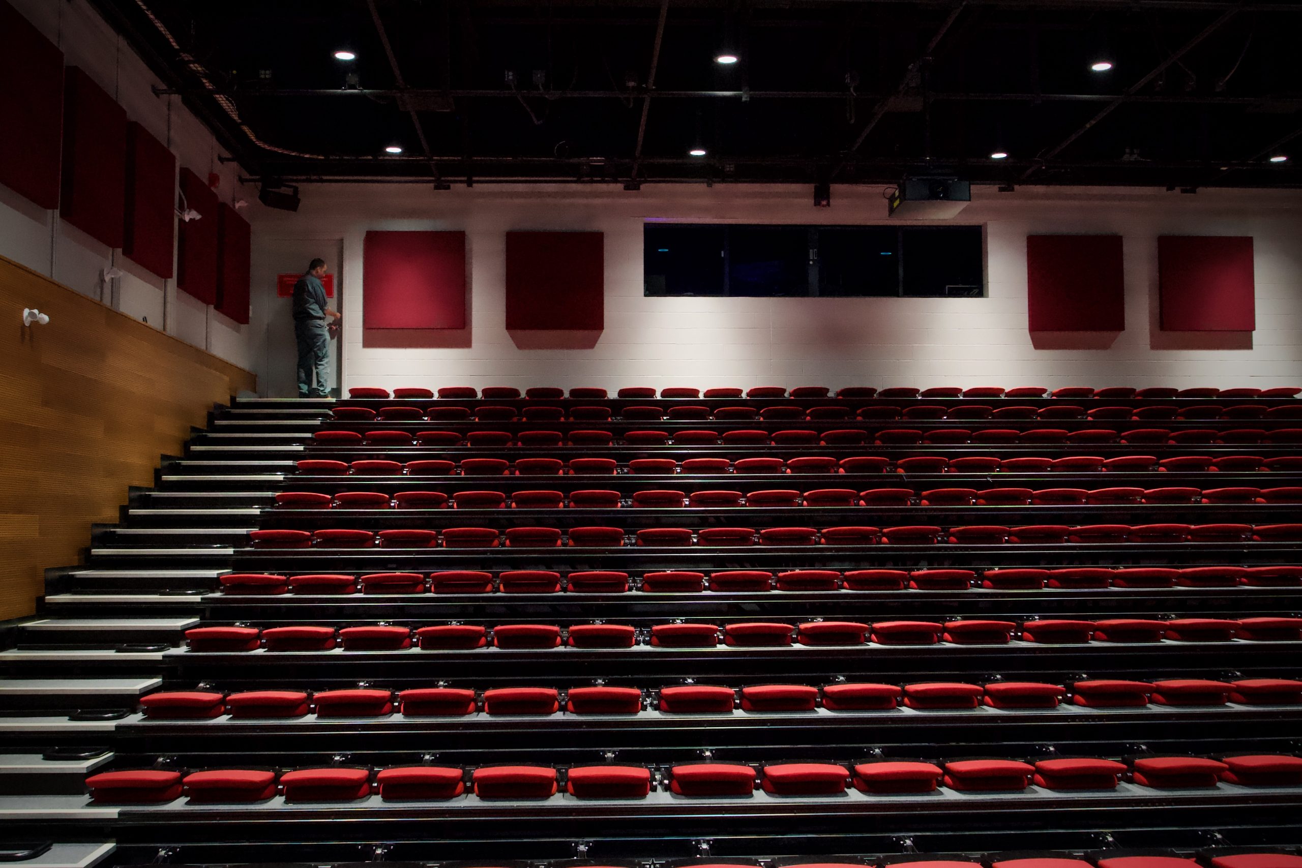 An empty auditorium's rows of seats. One man stands at the top.
