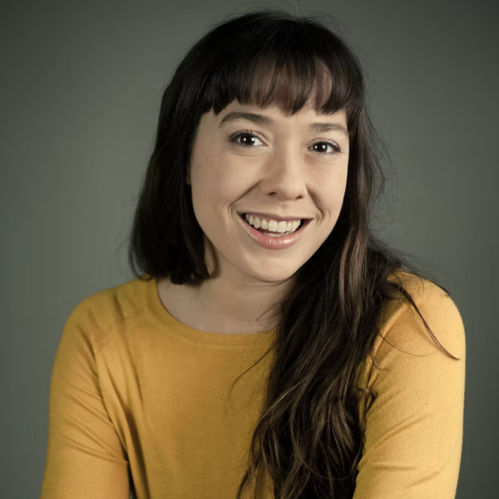 Woman with long brown hair wearing a yellow shirt smiling.