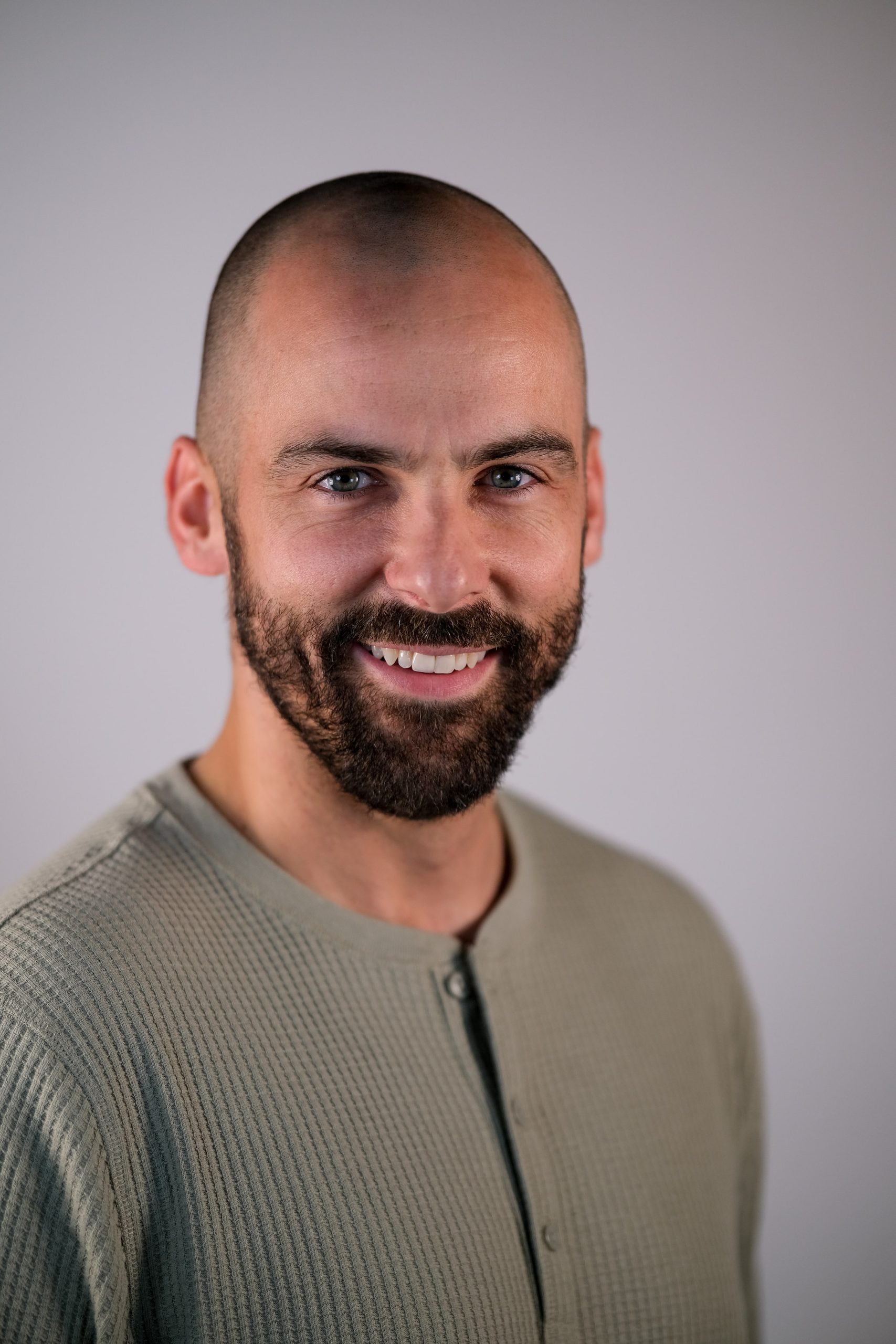 A man with a shaved head and beard smiles for the camera.