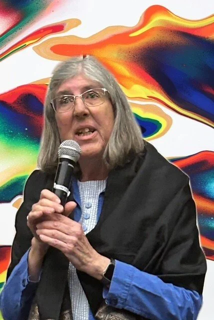 A woman with grey hair holds a microphone. Background is colourful and psychedelic.