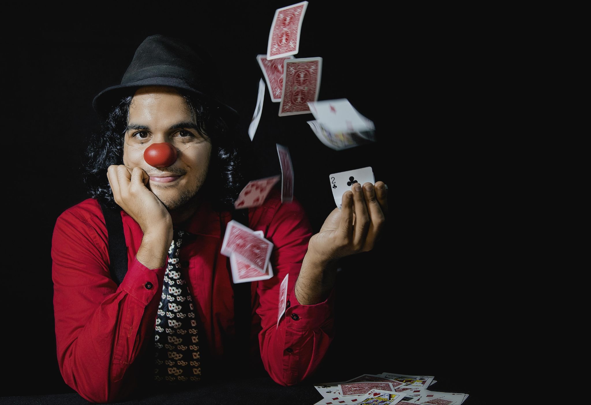 Man with clown nose and black top hat doing a card trick.