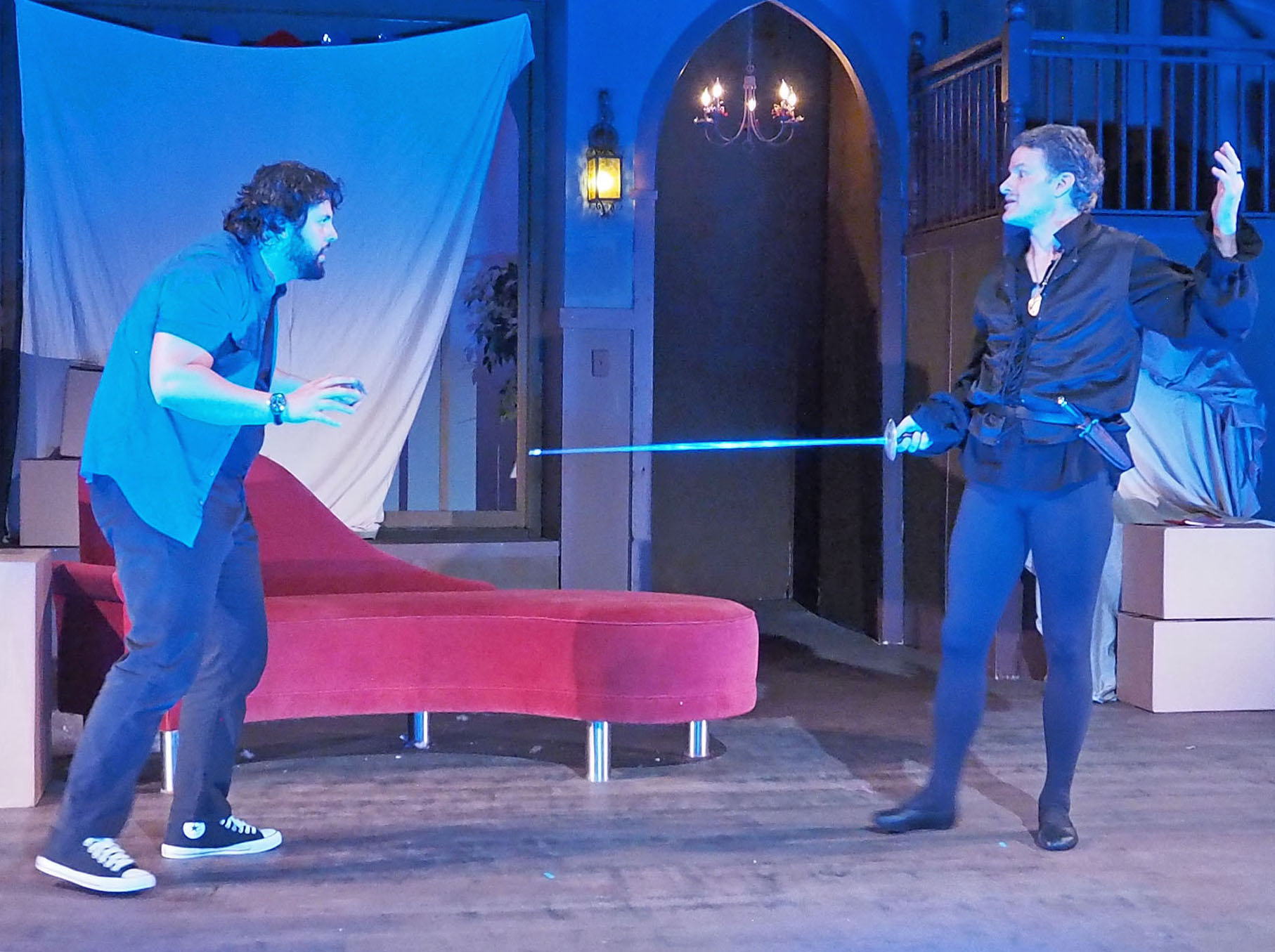 On the left, a man in modern clothes crouches. Across from him in the frame's right side, another man in costume brandishes a sword. 