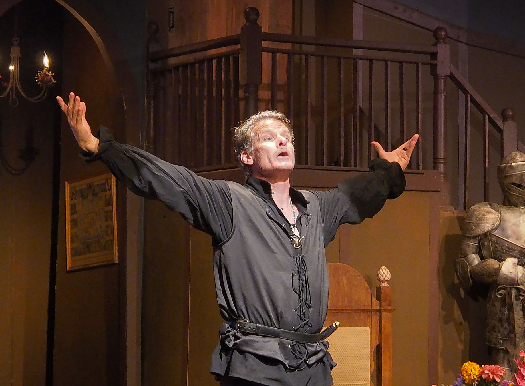 A man in renaissance costume stands in the middle of a stage with his arms outstretched in triumph.