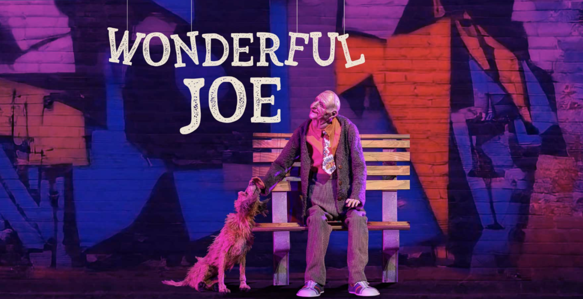 Text reading "Wonderful Joe" hovers suspended by marionette strings above puppet versions of an older gentlemen and his pet dog sitting on a park bench.