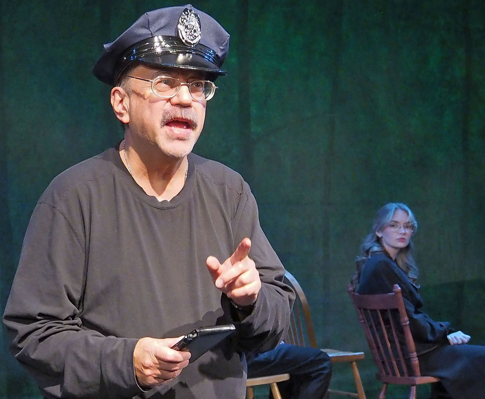Actor Barry Yuen speaks toward the audience wearing a police hat.