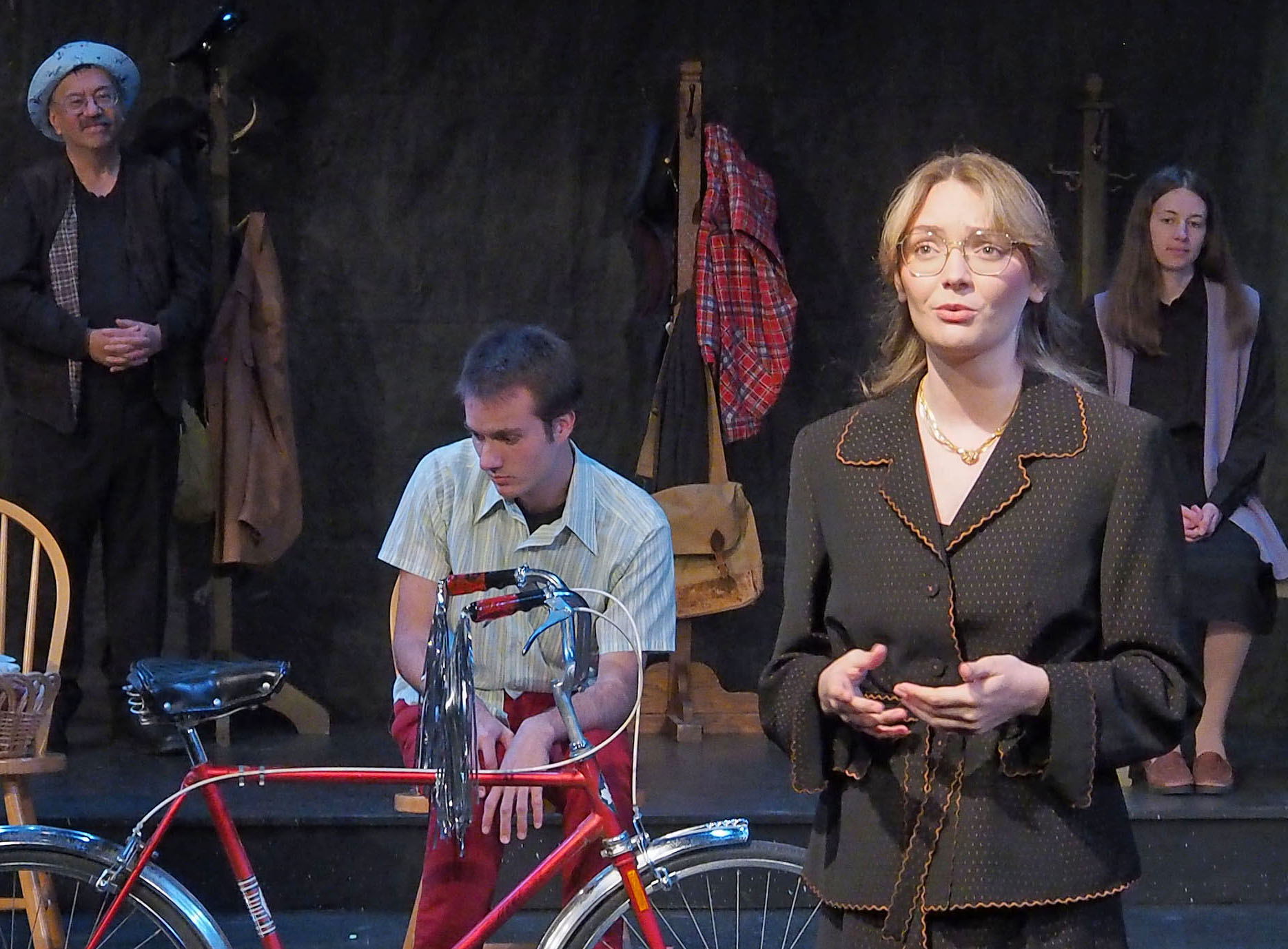 A collection of actors stands facing out, including Ian McGrath-Santowski as Steven Truscott seated and looking at the floor behind a rec bicycle.