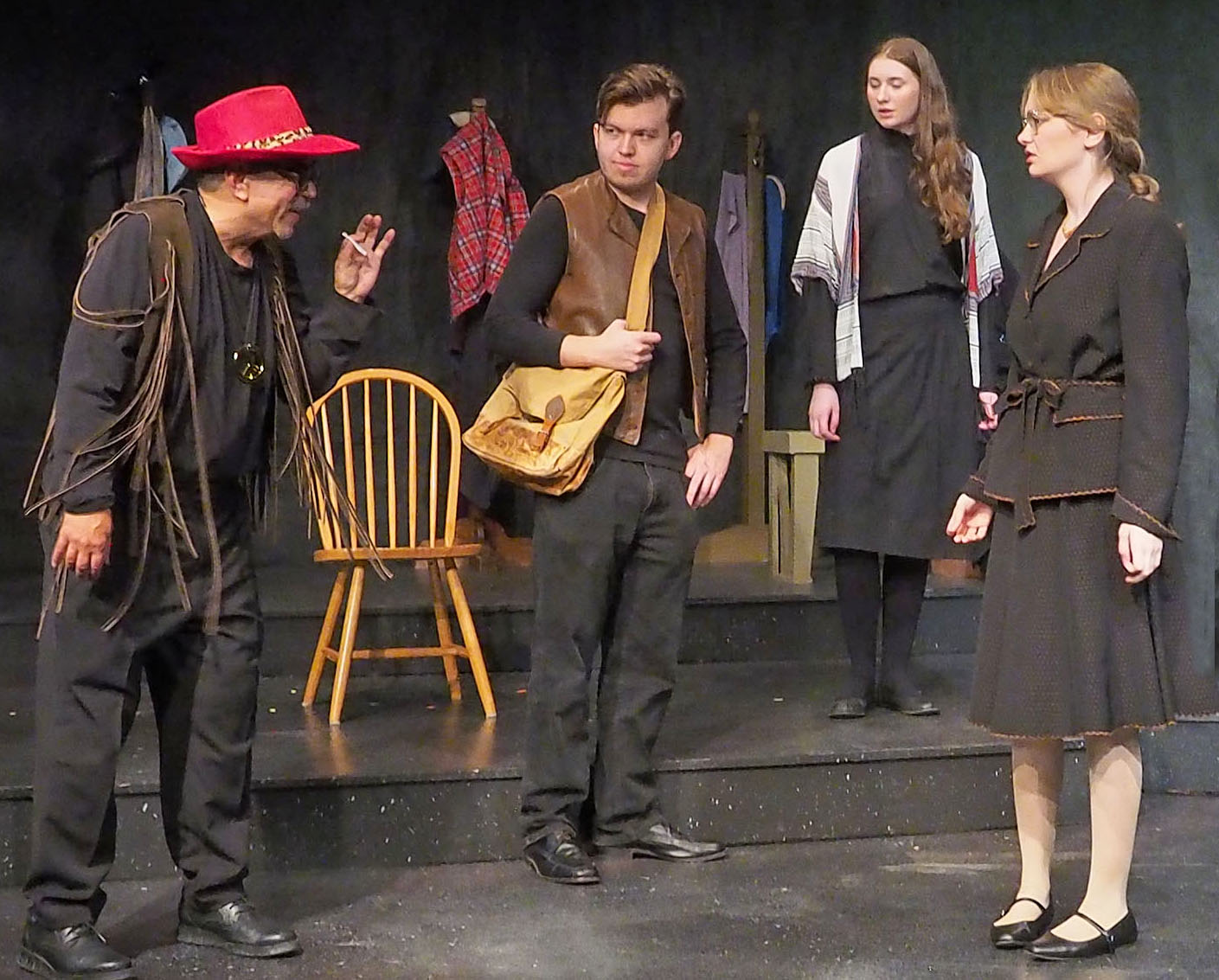 Barry Yuen, in a red cowboy hat with leopard-print trim and a suede fringe vest, leans forward to speak playfully at Ashley Miller, who is standing several feet away, unamused. Mitchell Mayne stands in the middle with a messenger bag over one shoulder.