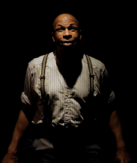 Cassel Miles, playing Josiah Henson, is illuminated by a spotlight as he looks upward.